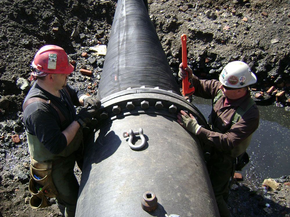 Crew members connecting a large pipe on a waterfront site